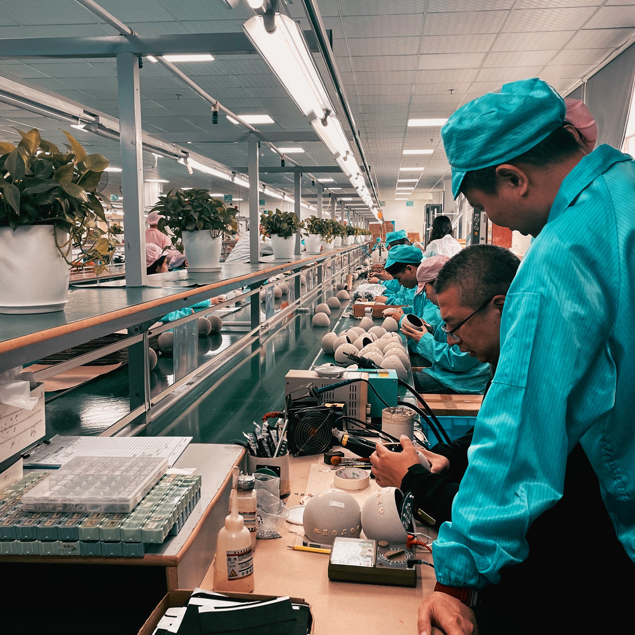 A panoramic view of the busy and clean HOUSBAY factory floor with multiple workers in blue uniforms collaborating on the assembly line.