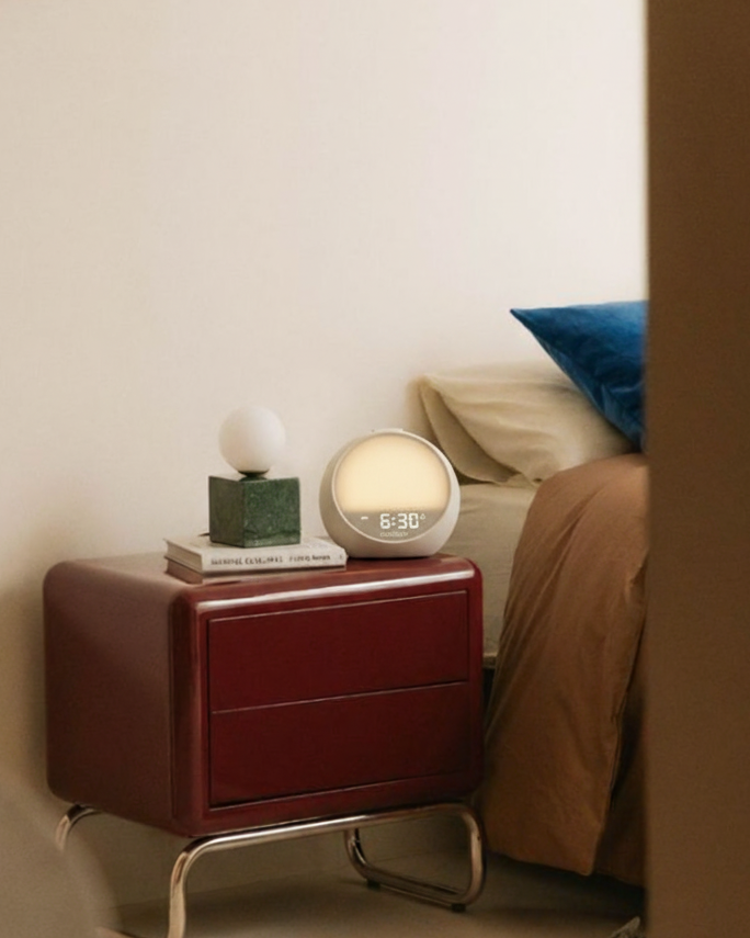 Rhythmana MINI glowing softly at 6:30 on a bedside table, in a small bedroom setup designed for gentle, screen-free mornings.